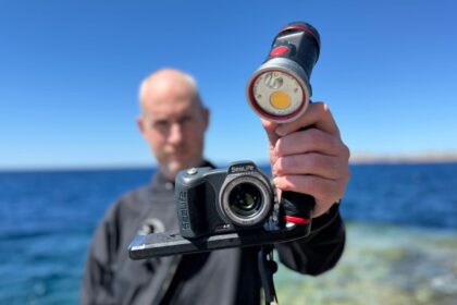 Our reviewer holding up the SeaLife Micro 3.0 camera and a video light on a tray by the sea