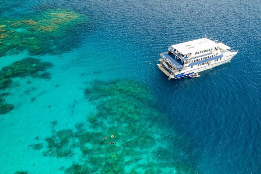 Aerial view of the OceanQuest catamaran anchored beside a turquoise reef with snorkelers in the water