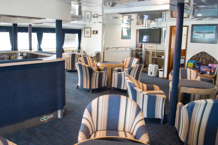 Lounge area on OceanQuest with striped armchairs, a TV and a shelf of dive books