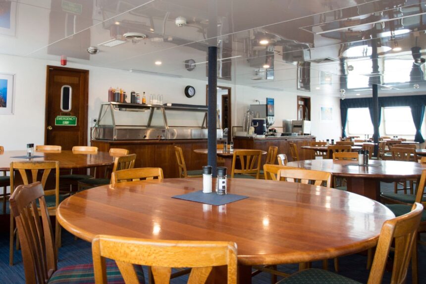 Dining room aboard OceanQuest set with round wooden tables and chairs