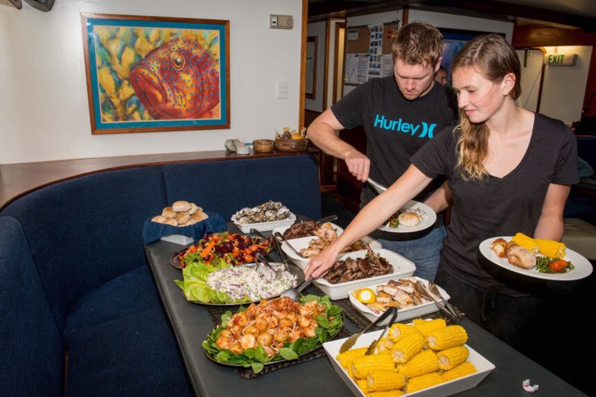 Crew members plating a buffet spread of seafood, corn and salads