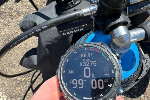 DIVEIN tester holding the Garmin Descent Mk3i in bright sun to check the AMOLED screen, dive gear behind