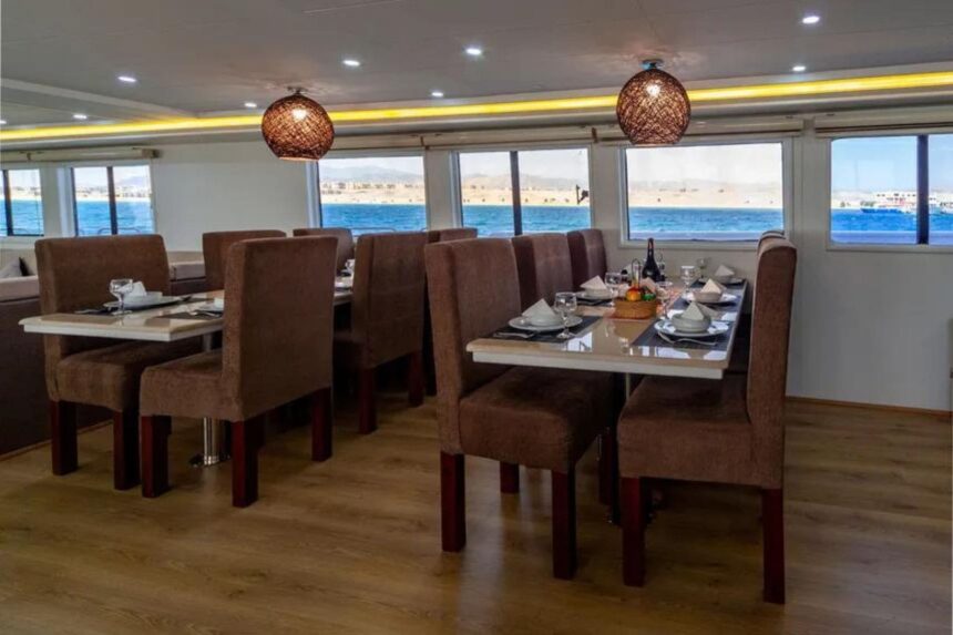 Dining tables set for guests beside large windows overlooking the sea