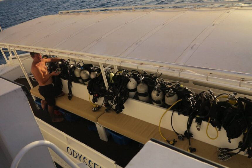 Crew member arranging scuba tanks racked along the boat's dive deck