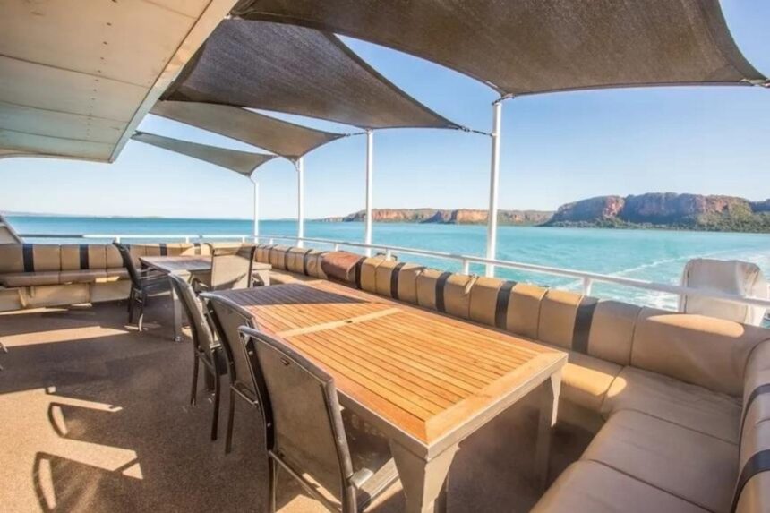 Wooden dining table set under shade sails with ocean view