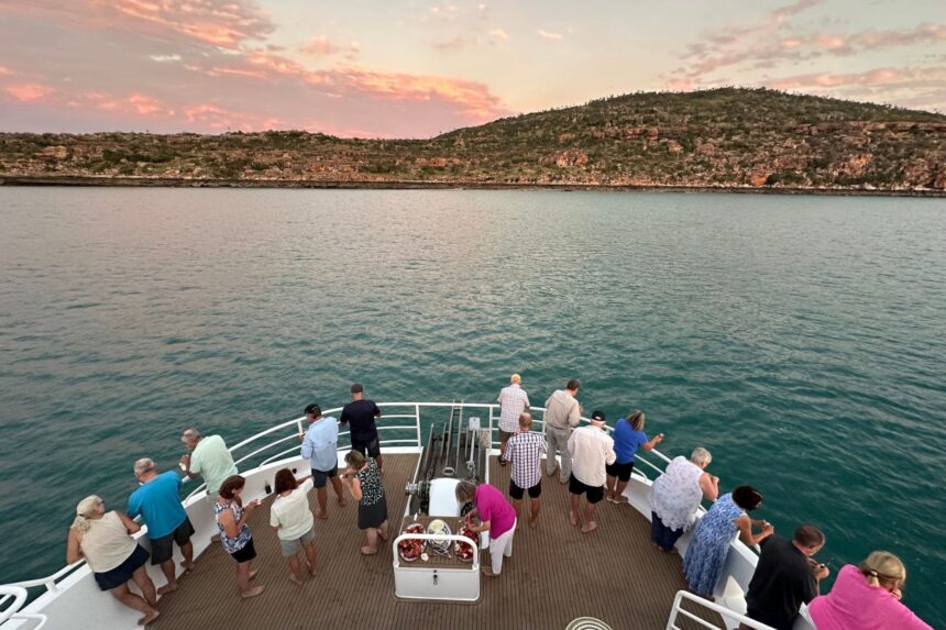 Guests standing along the bow rail watching a coastal sunset