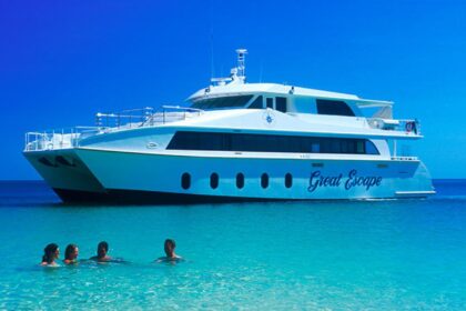 MV Great Escape liveaboard catamaran anchored in turquoise water with four swimmers nearby
