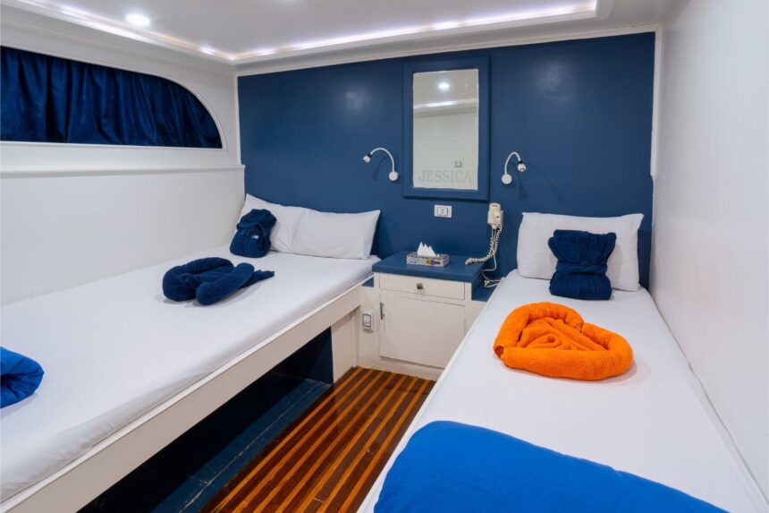 Twin cabin with blue accent wall and folded towels aboard Titan