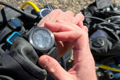 Our tester holding the round Shearwater Teric in both hands with dive gear laid out on the ground behind