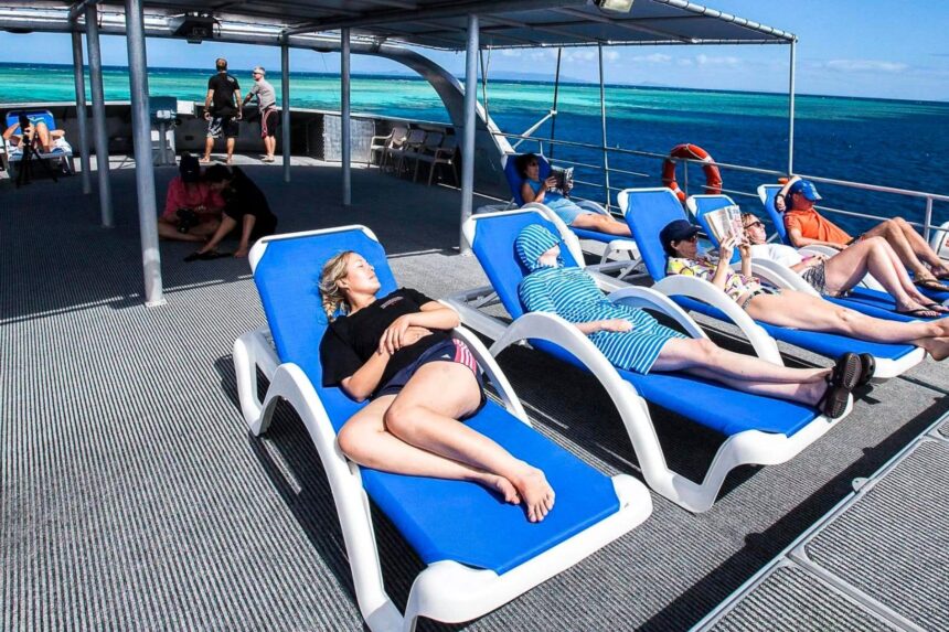 Guests relaxing on blue sun loungers aboard the Spoilsport with the reef visible below