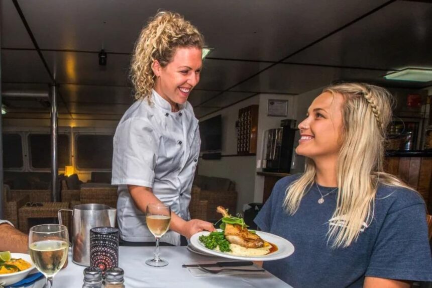 Crew member serving a plated dinner to a guest aboard the Spoilsport