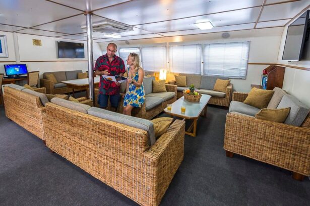Guests chatting over a brochure in the wicker-furnished lounge aboard the Spoilsport
