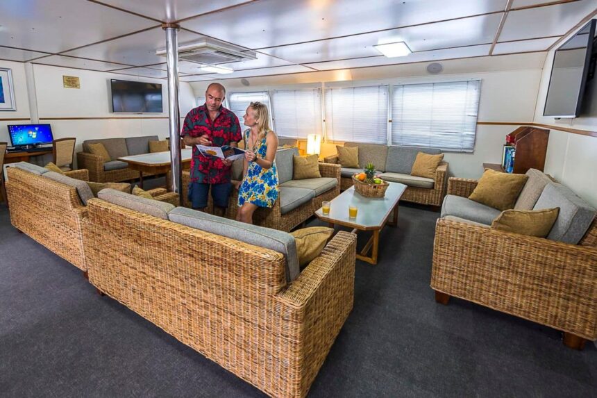 Guests chatting over a brochure in the wicker-furnished lounge aboard the Spoilsport
