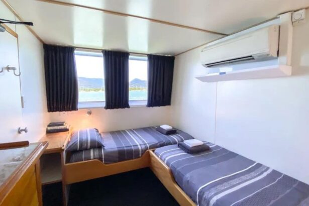 Twin-bed cabin aboard the Spoilsport with striped bedding and a wall-mounted air conditioner