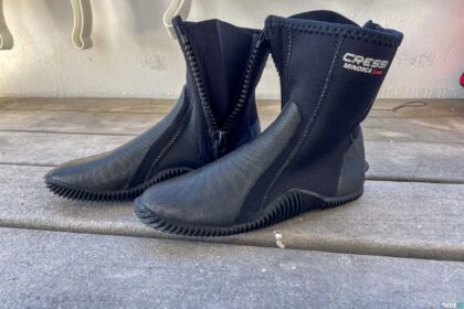 Pair of black Cressi Minorca 3mm neoprene dive boots with side zips and gripped soles on a concrete step