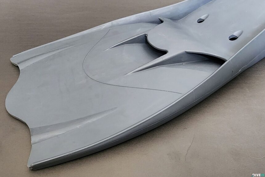 Black Hollis F1 LT fin propped at the edge of an indoor pool showing the spring strap and heel loop