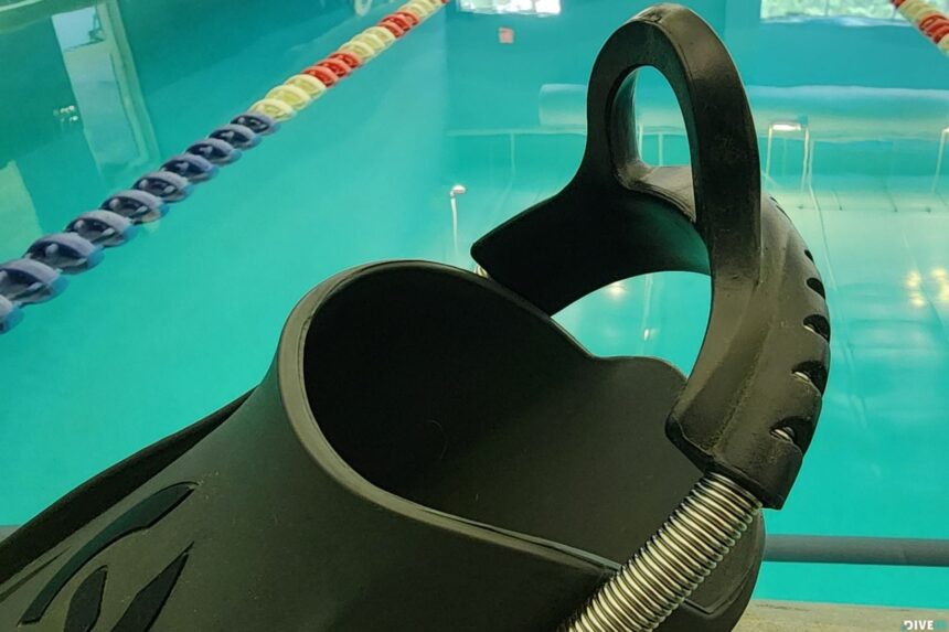Two Hollis fins standing against a scuba cylinder at the poolside, one with a steel spring strap