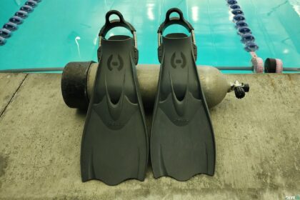 Hollis F1 LT fins standing upright against a scuba tank at the edge of a pool