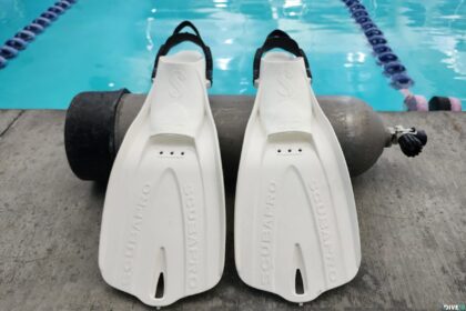White ScubaPro GO Travel fins leaning against a scuba tank on a pool deck