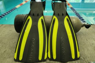 Black and yellow Oceanic Viper 2 open heel fins resting against a scuba tank beside a pool