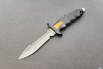 Akona Talon dive knife with black and yellow grip and part-serrated stainless blade on a grey surface