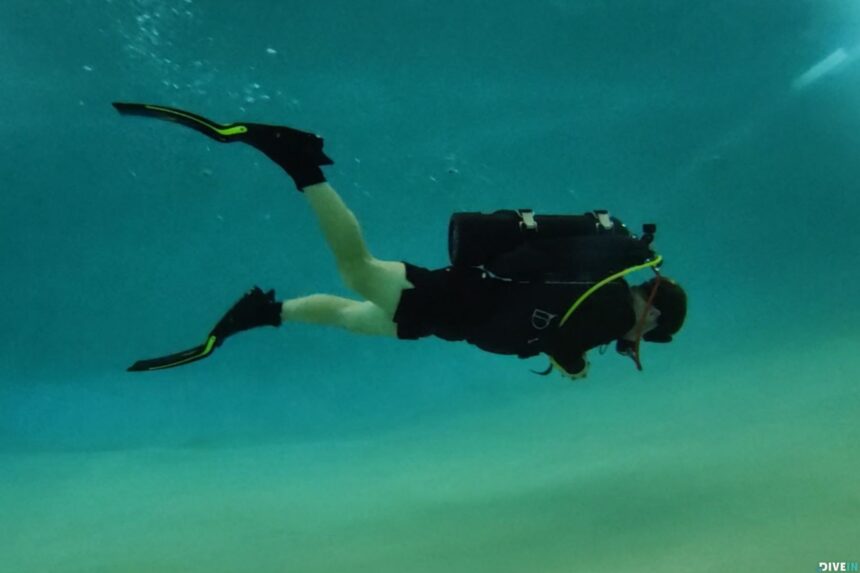 DIVEIN tester finning through a pool in a black wetsuit wearing the black and yellow TUSA Hyflex Switch fins