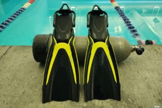 TUSA Hyflex Switch fins in black and yellow standing upright on a pool deck next to a scuba tank