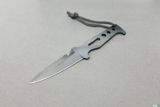 SEAC Tajaman dive knife with dark coated part-serrated blade and grey lanyard cord on a plain surface