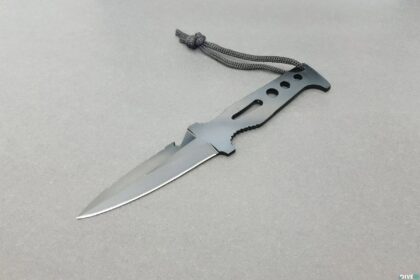 SEAC Tajaman dive knife with dark coated part-serrated blade and grey lanyard cord on a plain surface
