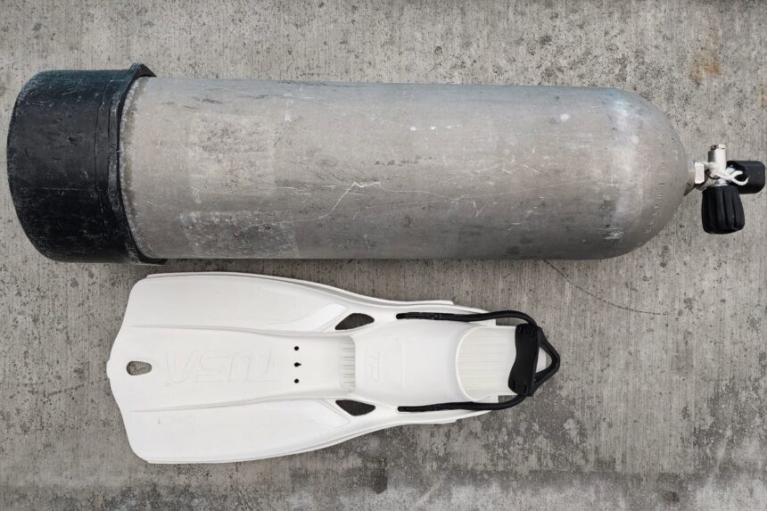TUSA Travel Right fin laid on the pool deck beside a scuba tank for scale