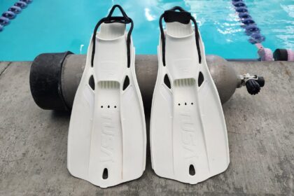 White TUSA Travel Right fins standing side by side on a pool deck beside a scuba tank