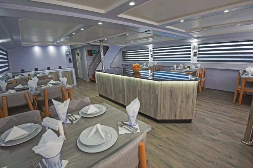 Dining area on the Blue Horizon liveaboard set with napkins and cutlery beside striped window blinds