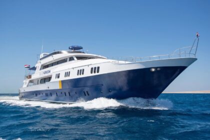 Blue Horizon liveaboard dive yacht cutting through open water at speed, flag flying at the stern