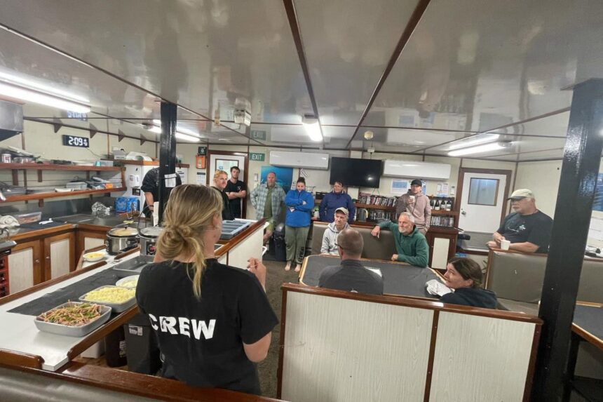 A crew member in a Rodney Fox shirt briefs guests seated in the saloon before a dive