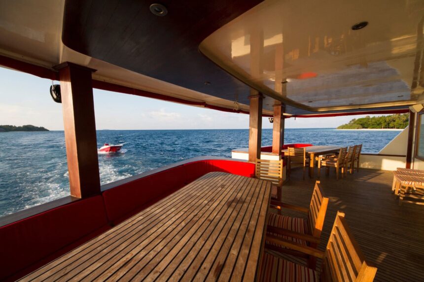 Covered dining table on MV Theia's deck with a tender boat visible offshore