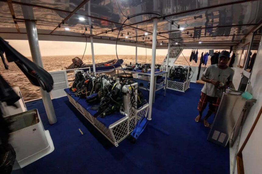 Dive tanks and gear staged on MV Oceania's dive deck at dusk with a crew member nearby