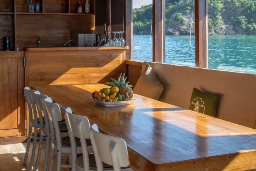 Wooden dining table set with a fruit bowl beside teal water views on the Indo Master