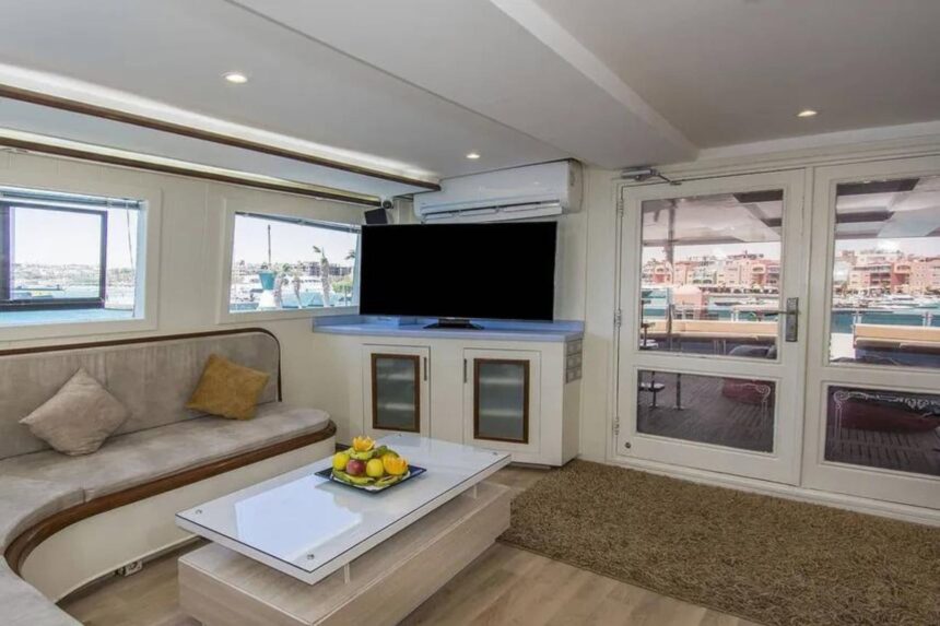 Indoor lounge with a sofa and TV aboard the Sea Serpent Contessa, marina visible through the doors