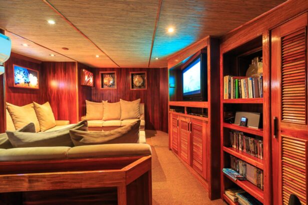 Lounge with sofas, a wall-mounted TV and a shelf of books and DVDs on the Ocean Hunter III