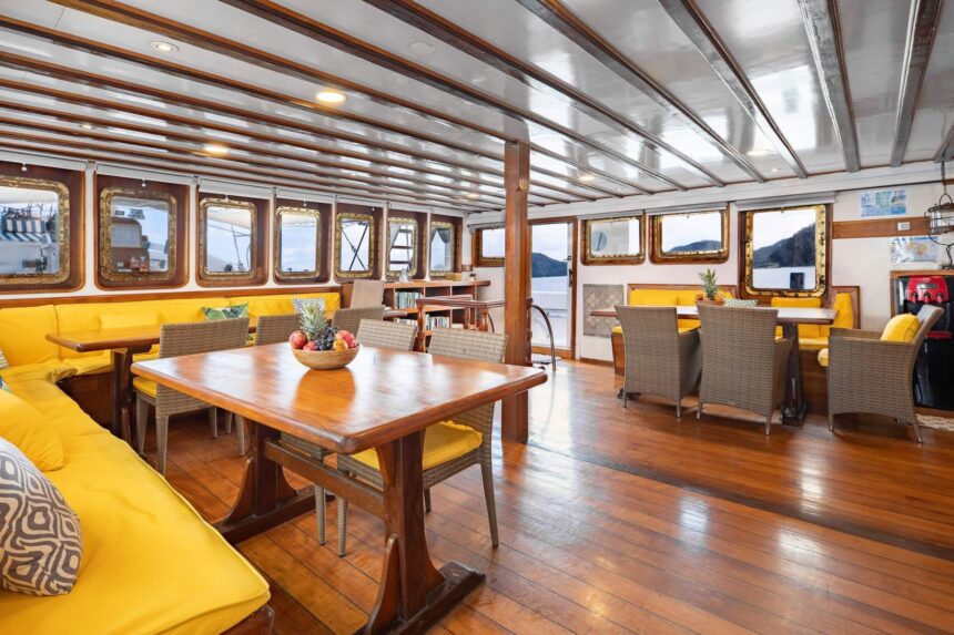 Dining area on the MSY Seahorse with a wooden table, yellow cushioned seating and porthole windows