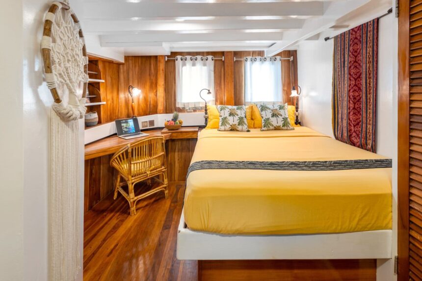 Cabin with a yellow bedspread, palm-print pillows and a small desk on the MSY Seahorse