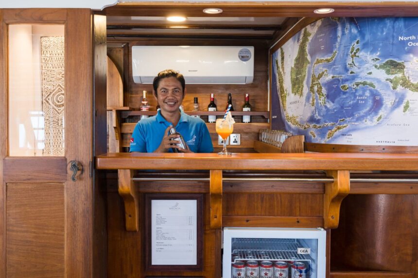 Bartender mixing a cocktail behind the bar on the MSY Seahorse with a regional dive map on the wall