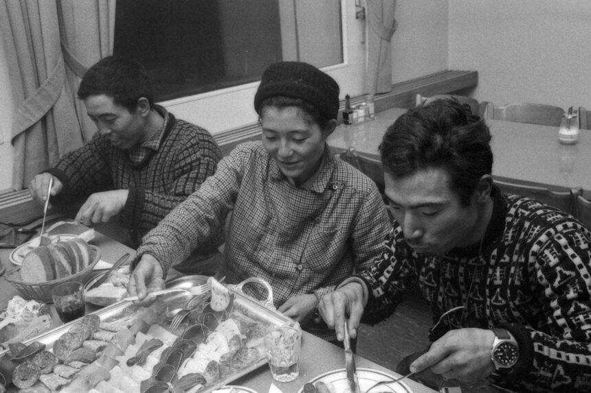 Black and white archive photo of three Japanese mountaineers eating a meal, one wearing a wristwatch
