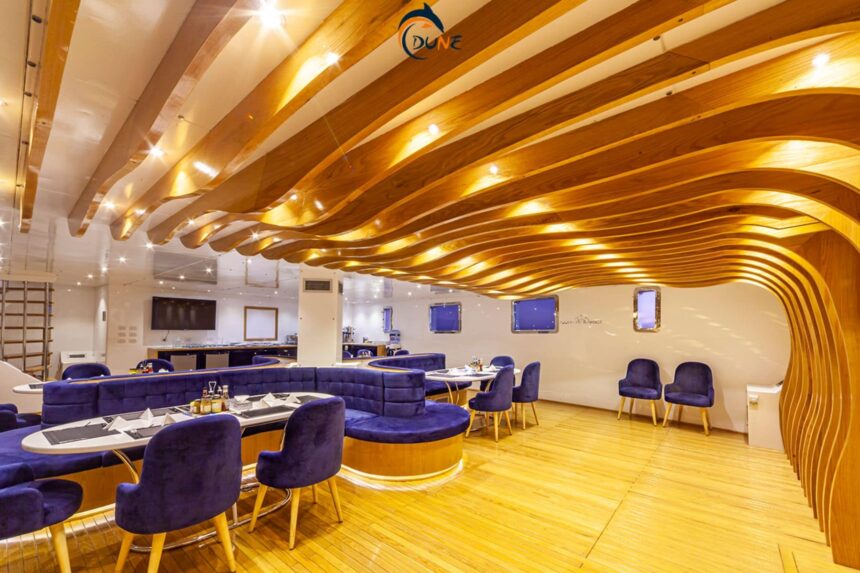 Dining room aboard the Alia liveaboard with a wave-patterned wood ceiling