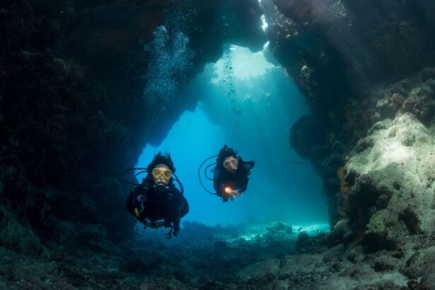 Two divers hovering inside an underwater cavern lit by shafts of sunlight