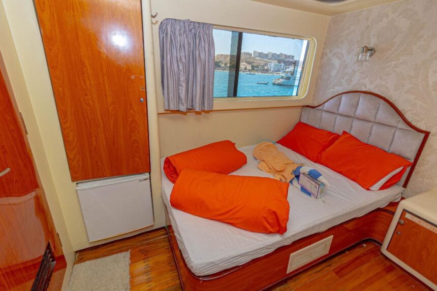 Cabin aboard the Betel Gueser with orange bedding and a harbor view