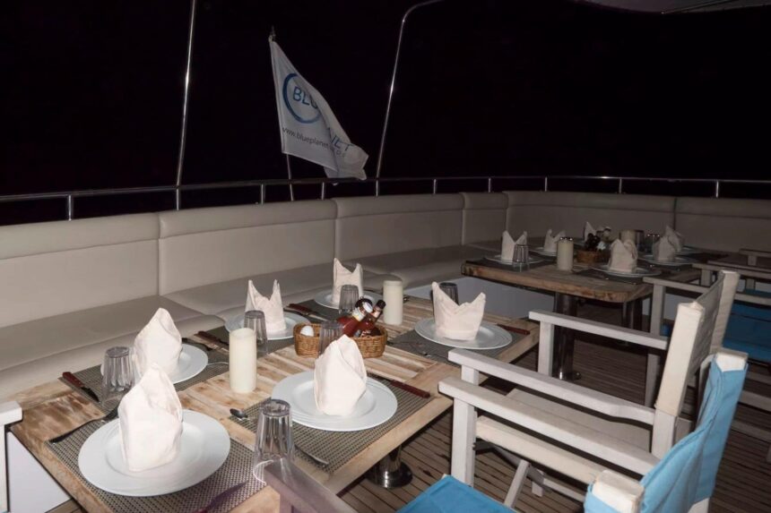Dinner tables set with white napkins on the open deck of the MY Blue Seas at night