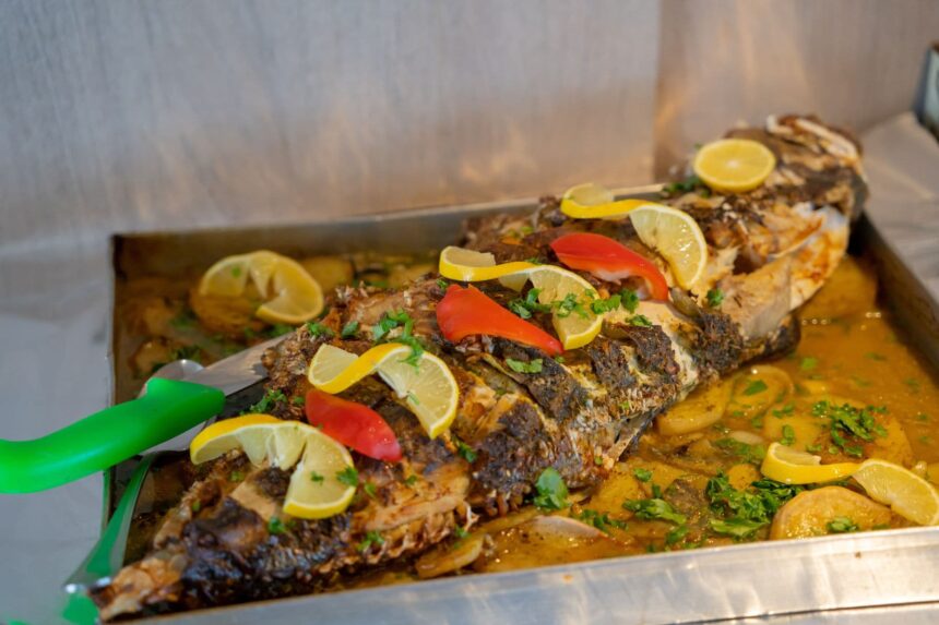 Whole grilled fish garnished with lemon and peppers served on a metal tray