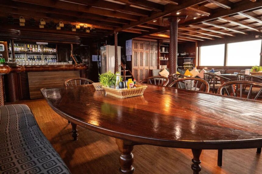 Wooden dining table with bar and bookshelf in the salon aboard the Amba