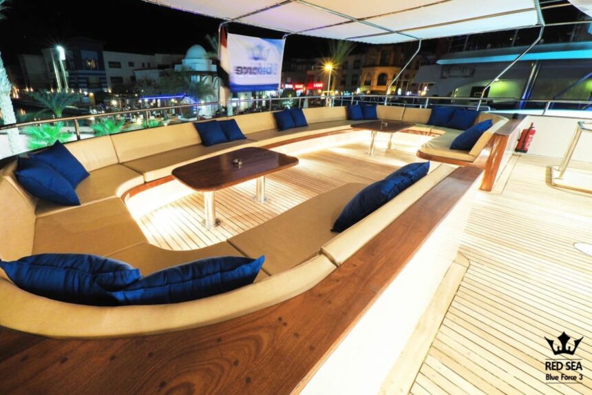 Lit outdoor lounge deck with blue cushioned seating aboard the Blue Force 3 at night